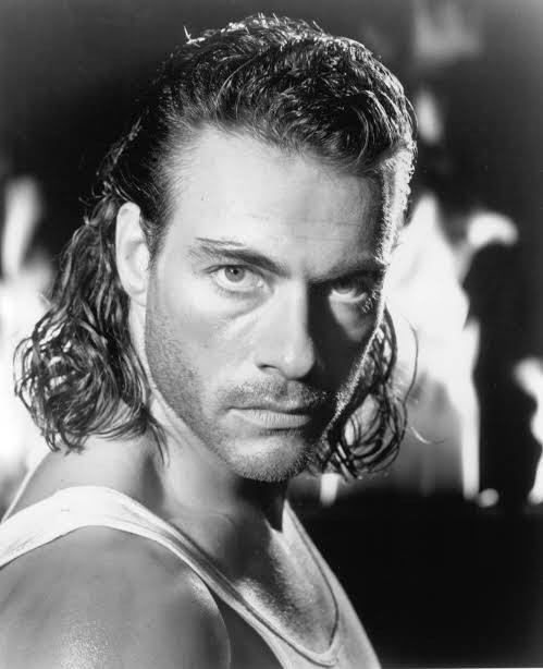 Portrait en noir et blanc de Jean-Claude Van Damme, cheveux mi-longs, regard de face